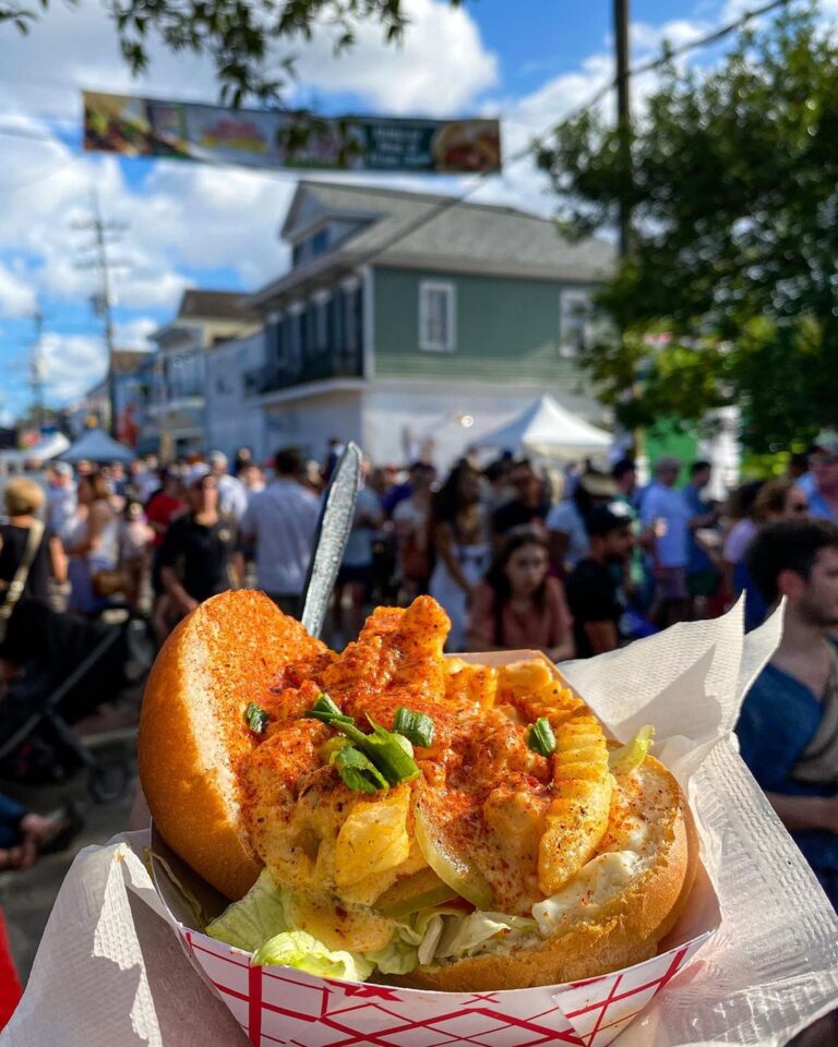 A delectable poboy held high with festive Oak Street revelry in the background